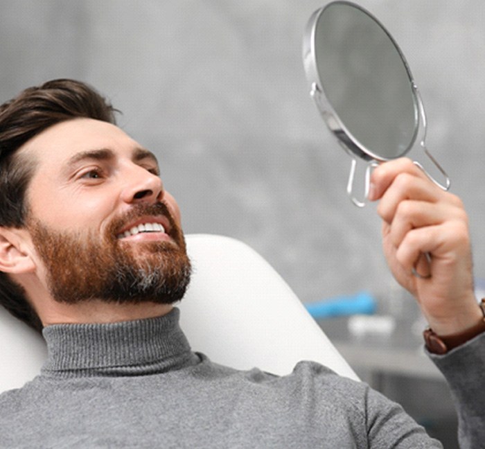 A patient in Waverly, OH smiling at their new dental crown in a mirror