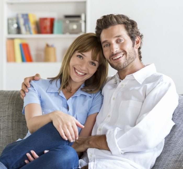 Man and woman smiling on couch after seeing emergency dentist in Waverly