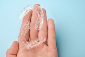 Hand holding 2 clear aligners over light blue surface